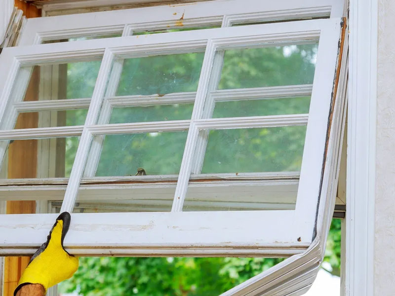 Gloved hands removing an old wooden window frame from a house opening. 
