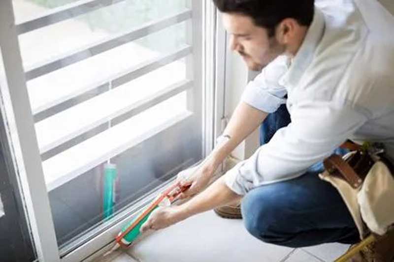 Person applying sealant along the bottom track of a sliding glass door.