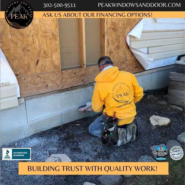 Worker in a yellow Peak Windows and Doors hoodie repairing the exterior wall of a house.