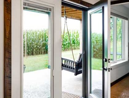 Open glass patio door leading to a covered outdoor area with a swing and a view of tall corn plants.