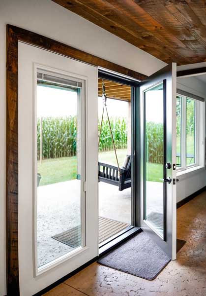Open glass patio door leading to a covered outdoor area with a swing and a view of tall corn plants.
