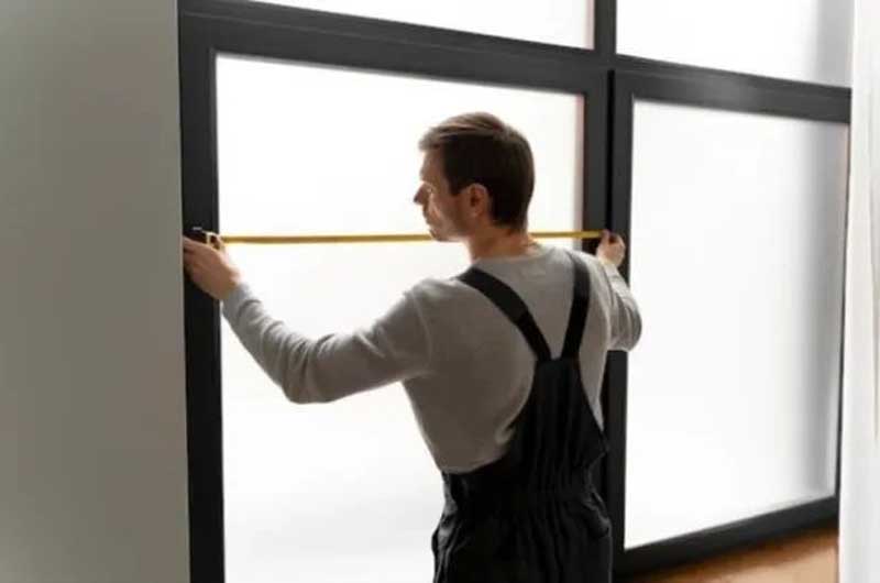 Person measuring the width of a large window frame using a tape measure.
