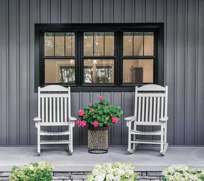 Front porch with two white rocking chairs and a potted flower arrangement in front of a black‑trimmed window.