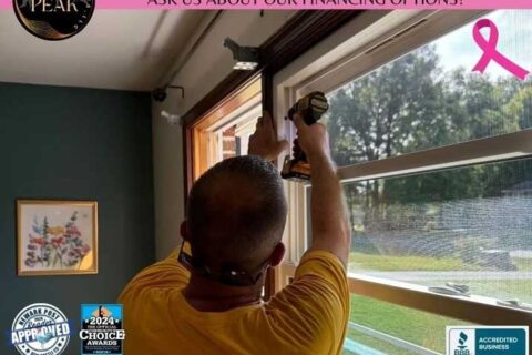 Person installing or adjusting a window frame using a power drill inside a room.