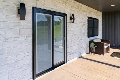 Sliding glass patio door with built-in blinds on a stone exterior wall beside a small outdoor seating area.