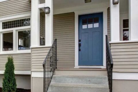 Front porch with a blue paneled door, white trim, beige siding, and black metal railings along the steps.