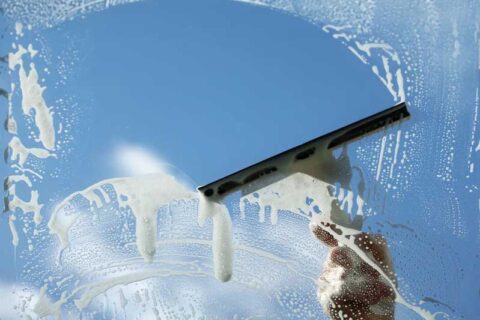 Squeegee wiping soapy water from a window against a clear blue sky.