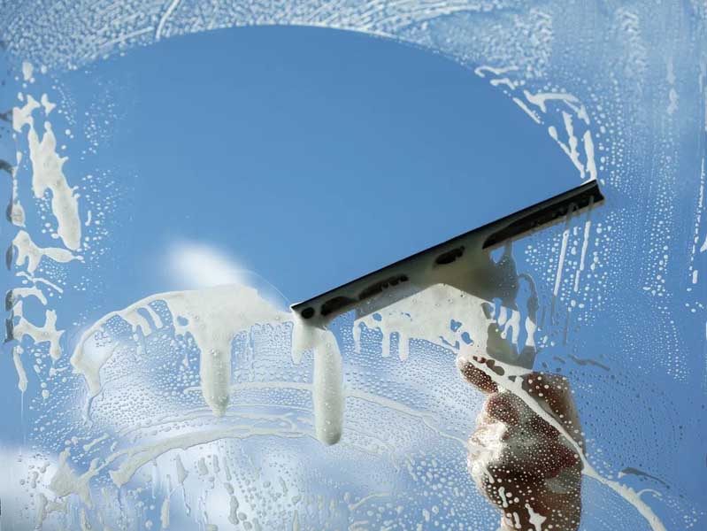 Squeegee wiping soapy water from a window against a clear blue sky.