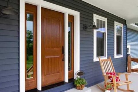 Front porch with a wooden door, sidelights, blue siding, and a rocking chair with a red pillow.