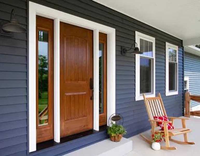 Front porch with a wooden door, sidelights, blue siding, and a rocking chair with a red pillow.