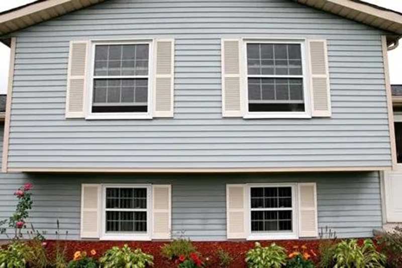 House exterior with blue siding, white-trimmed windows, shutters, and a landscaped garden bed.