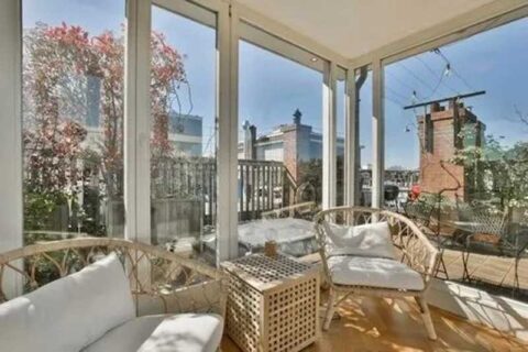 Sunroom with wicker furniture and large glass windows overlooking a patio and cityscape.