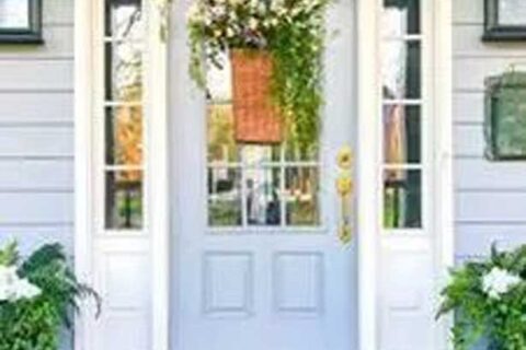 Front door with sidelights, floral basket décor, welcome mat, and potted plants on each side.